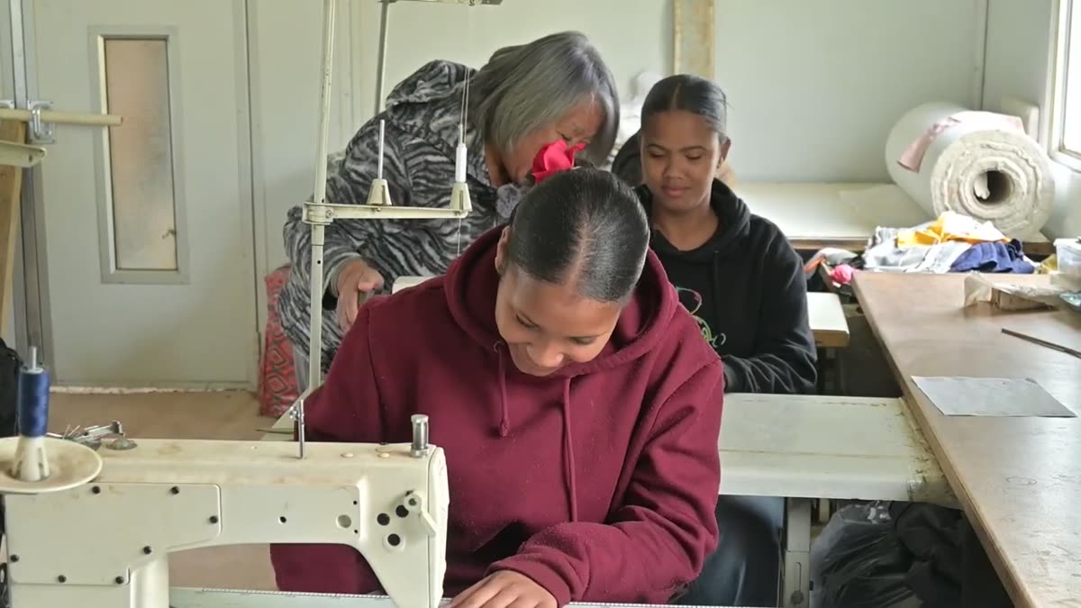 Young women learning to sew on industrial sewing machines with their trainer